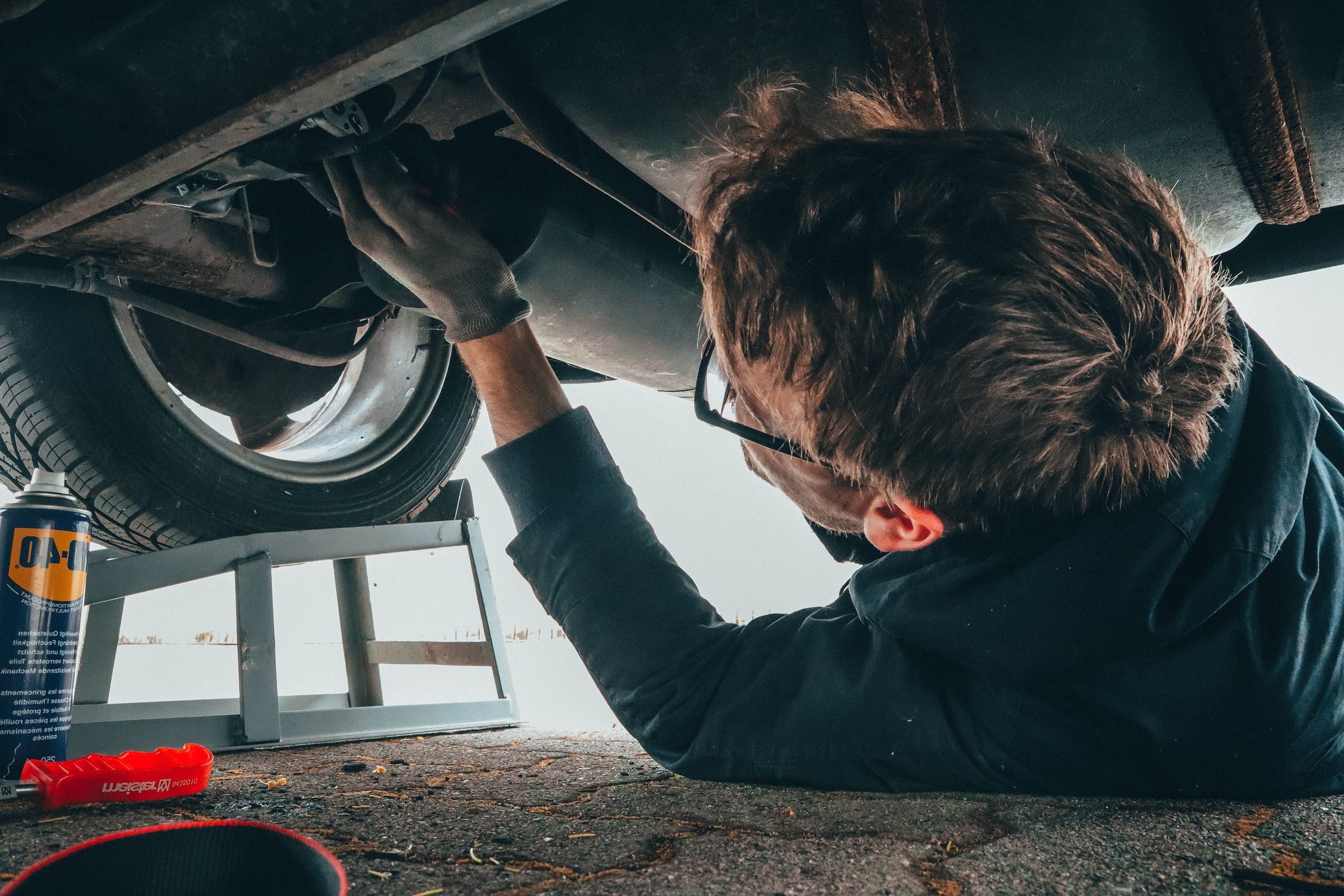 Specialty Automotive mechanic working on the underneath of a vehicle with WD-40 spray